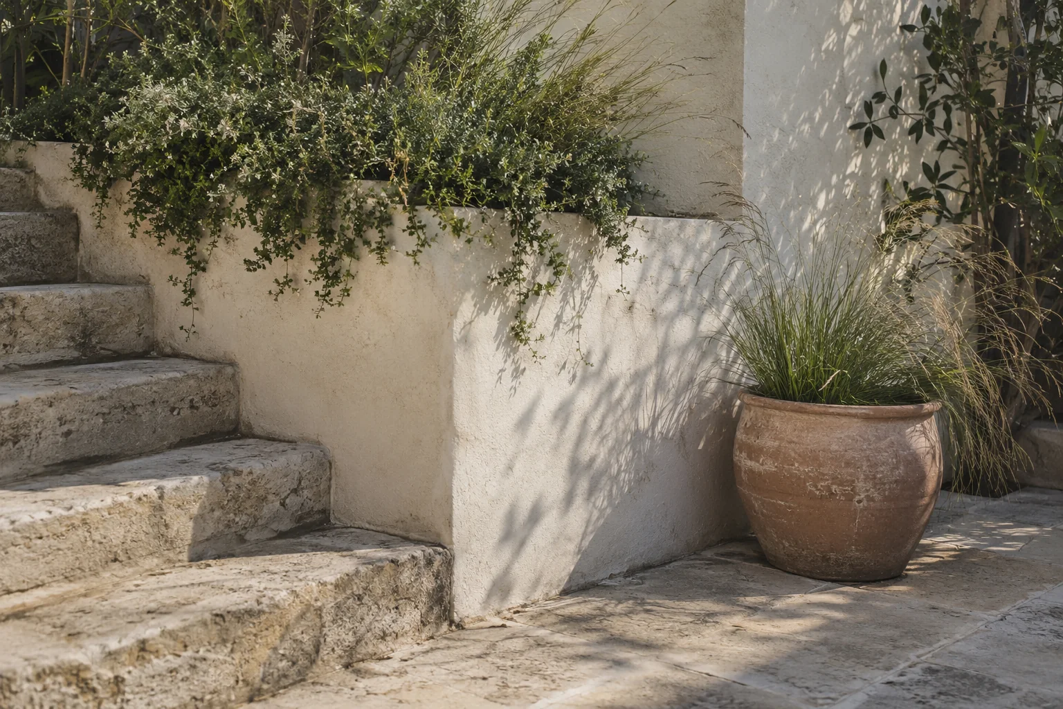 Stone steps, a plaster wall and a terracotta pot beside garden planting.