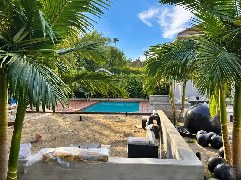Poolside garden during construction, with prepared ground and an unfinished concrete planter before turf installation.