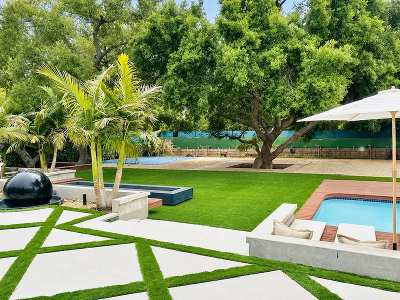 Poolside garden with geometric pale paving, lawn, palms and planted areas beside the pool.