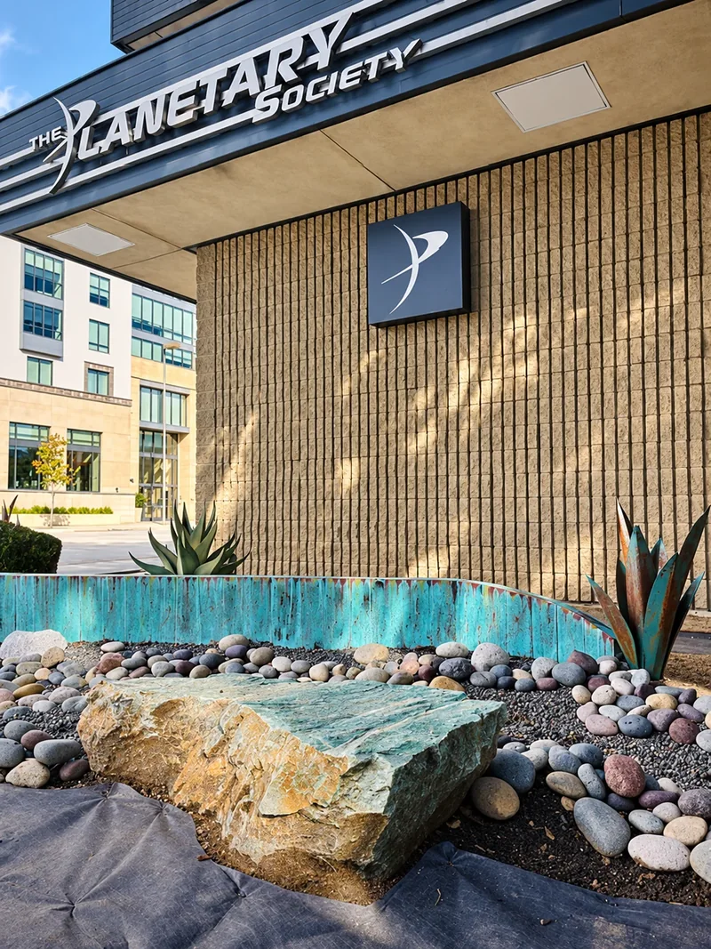 A boulder and rounded river stones beside turquoise planter walls at The Planetary Society.