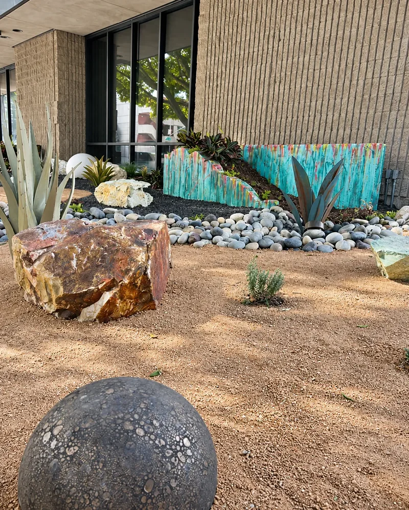 Turquoise planter walls behind boulders and a dark sphere set in gravel.