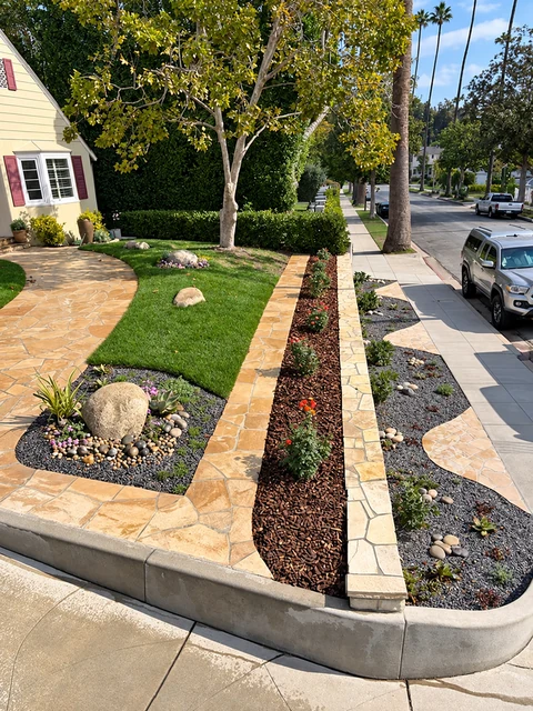 Residential parkway with a low stone retaining edge, lawn, boulder, and planting strip.