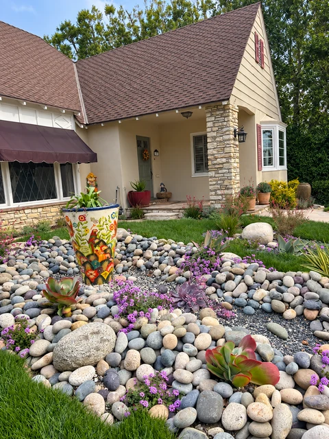 Colorful Talavera vessel surrounded by river stones and flowering plants in a front garden.