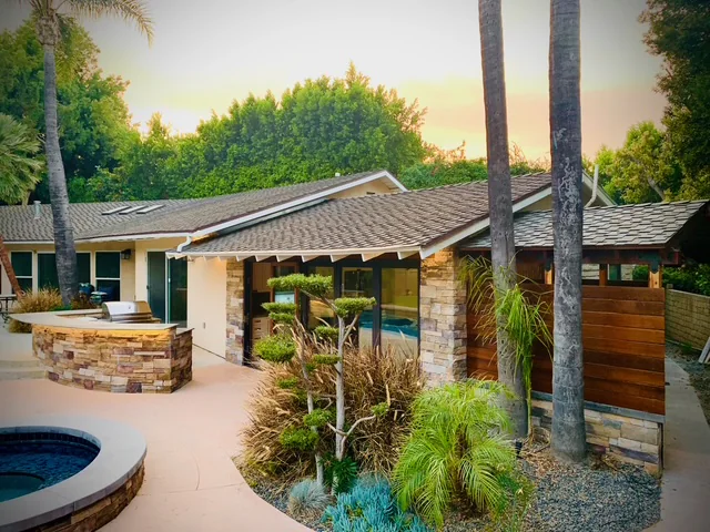 Poolside garden and pool-house roofline framed by palms and mature trees in Encino.