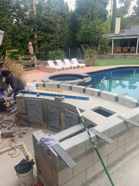 Curved BBQ island layout marked with masonry blocks beside a kidney-shaped swimming pool.