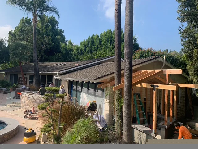 Outdoor kitchen and shower structures being built beside the pool and mature trees.