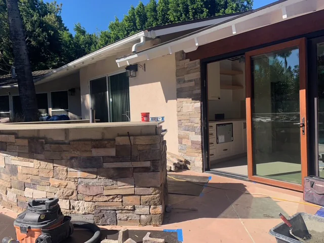 Stone veneer being installed at the outdoor BBQ area and pool-house entrance.