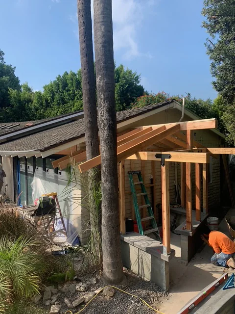 Outdoor shower framing under construction beside mature trees and the pool.