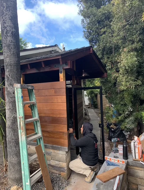 Outdoor shower structure with hardwood boards and stone veneer during installation.