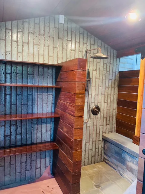 Outdoor shower interior with stacked subway tile, hardwood shelves, and warm pendant lighting.