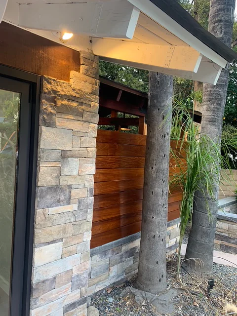 Red Balau outdoor-shower slats beside stacked-stone veneer and the pool-house wall.