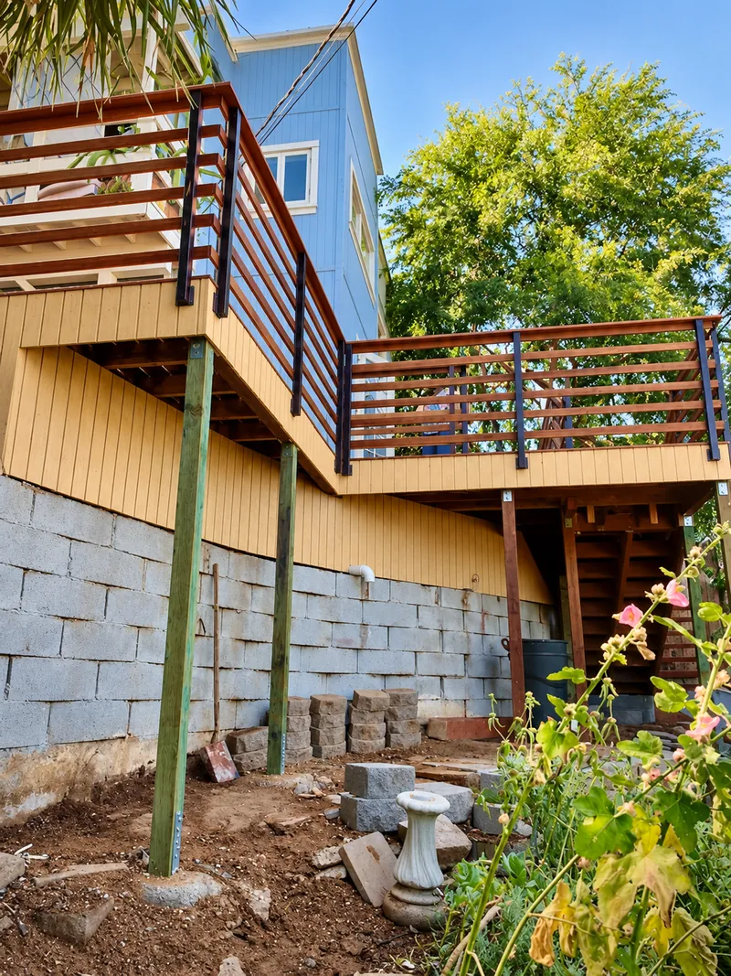 Raised timber deck and railings above a block retaining wall, with support posts and ground below.