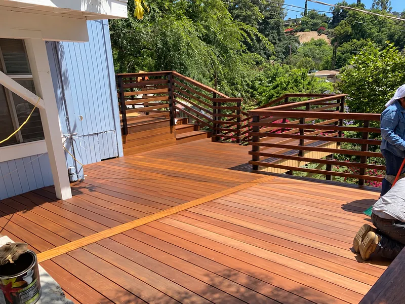 Timber deck during installation, with a worker beside the new boards and railings.