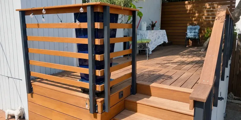 Timber deck with dark metal railing posts, horizontal wood rails, string lights, and seating.