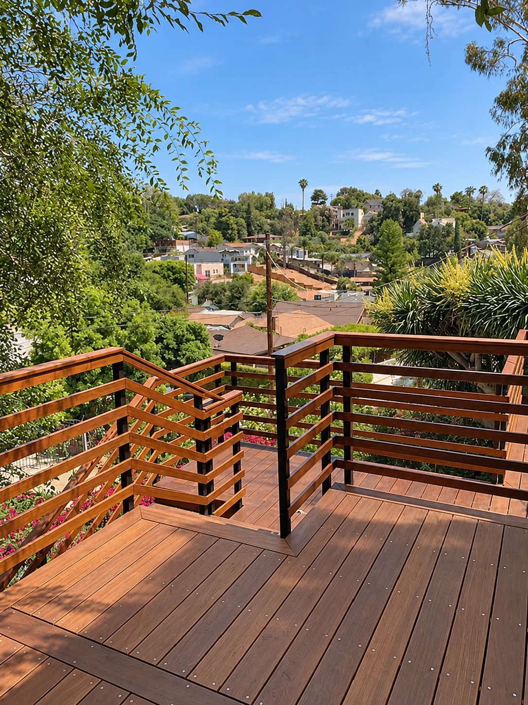 Timber deck with layered railings, stairs, mature trees, and a view over nearby homes.